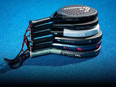 Plusieurs raquettes de padel de différentes marques empilées sur un terrain bleu pour bien choisir sa raquette